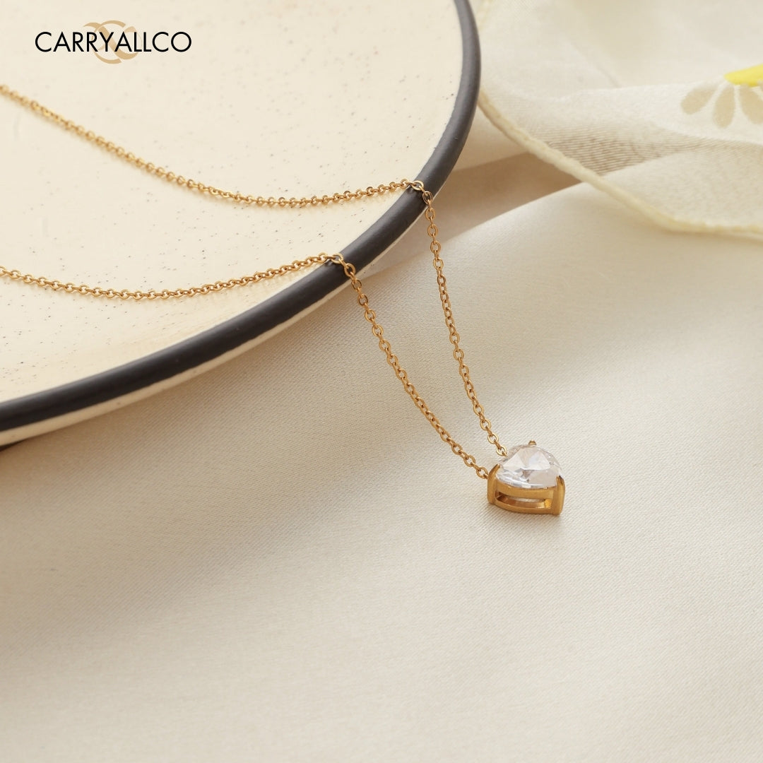 Gold necklace with a heart-shaped pendant on a light background, featuring the brand 'CARRYALICO'.