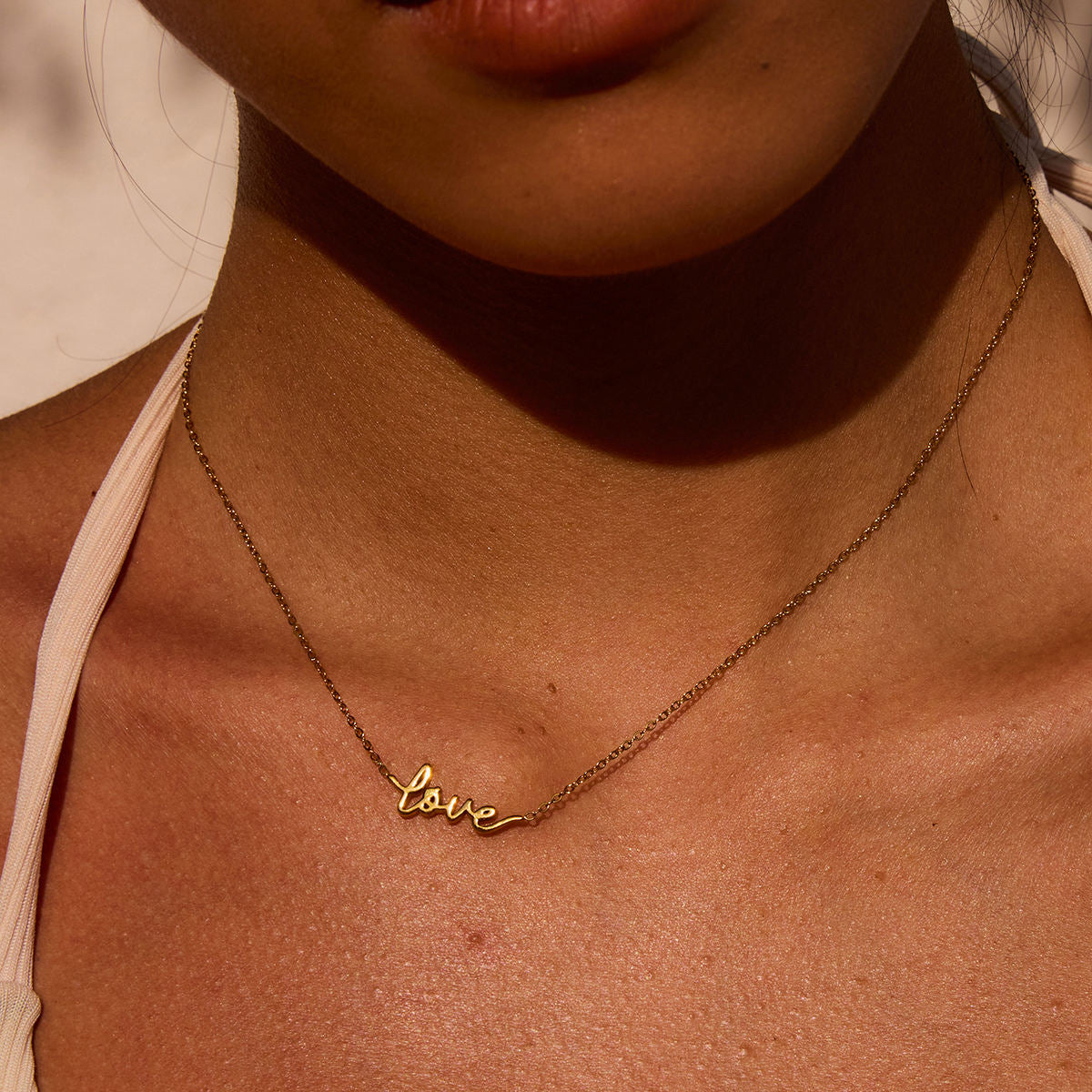 Gold 'love' necklace on a person's neck with a neutral background