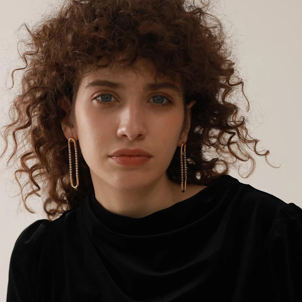 Woman with curly hair wearing gold hoop earrings against a neutral background