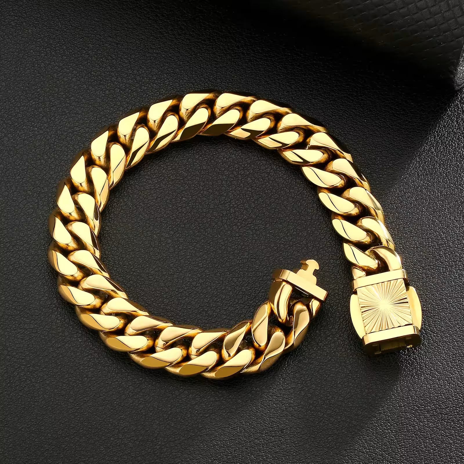 A thick gold Cuban link chain bracelet with a square sunburst-patterned clasp, displayed on a textured black surface.