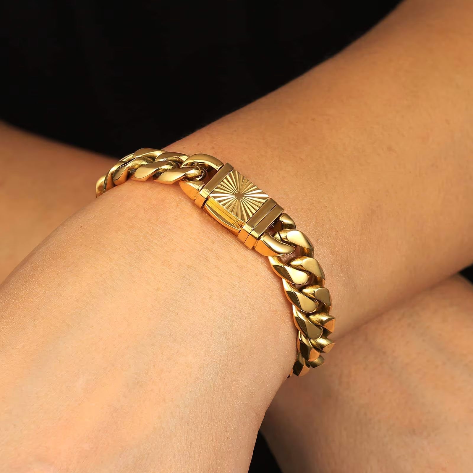 A gold-toned chunky Cuban link bracelet with a sunburst clasp, shown worn on a person's wrist against a dark background.