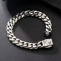 A silver-toned Cuban link chain bracelet with a square sunburst clasp, displayed on a textured black surface.