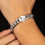 A close-up of a silver-toned metal chain bracelet with a sunburst clasp, worn on a person's wrist against a dark background.