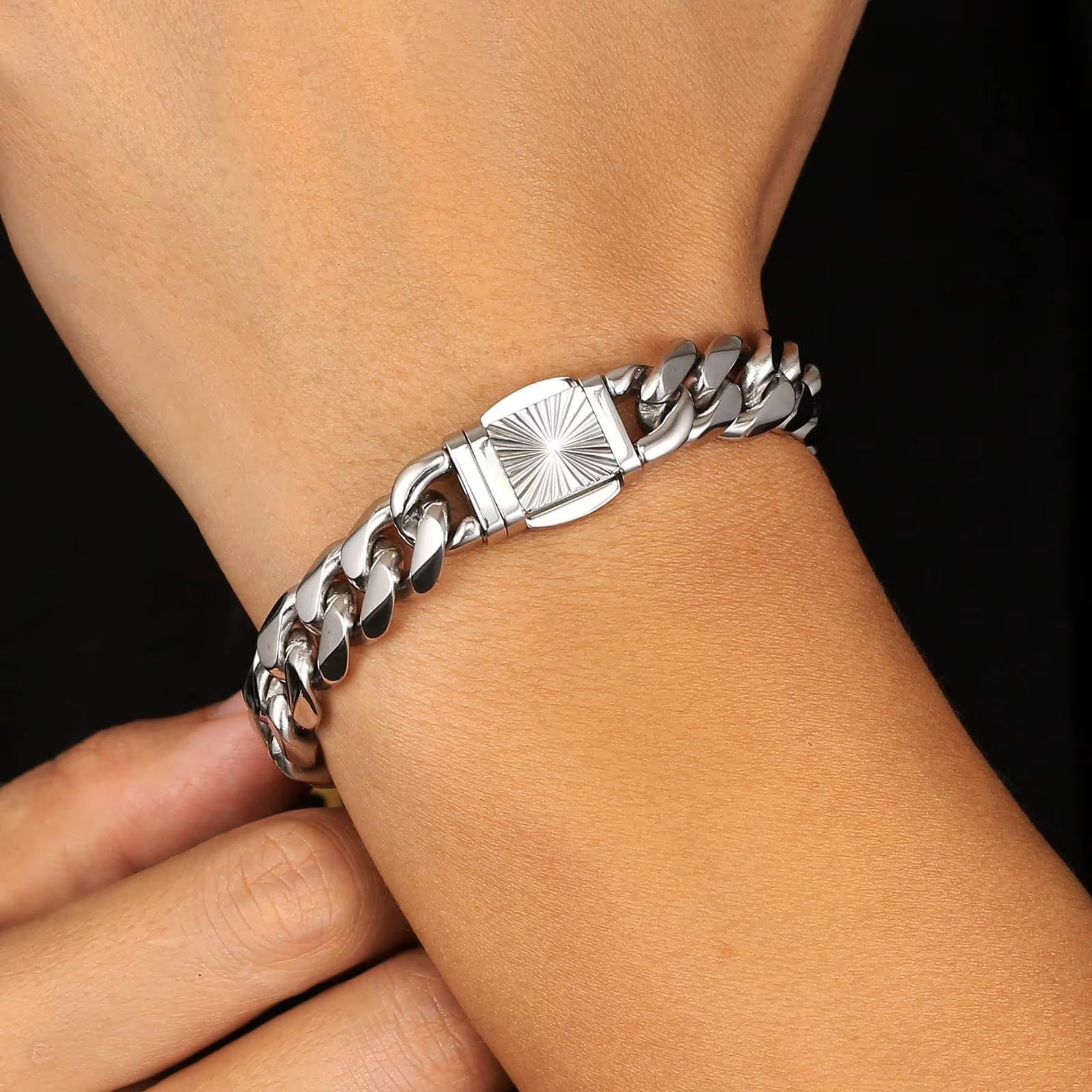 A close-up of a silver-toned metal chain bracelet with a sunburst clasp, worn on a person's wrist against a dark background.