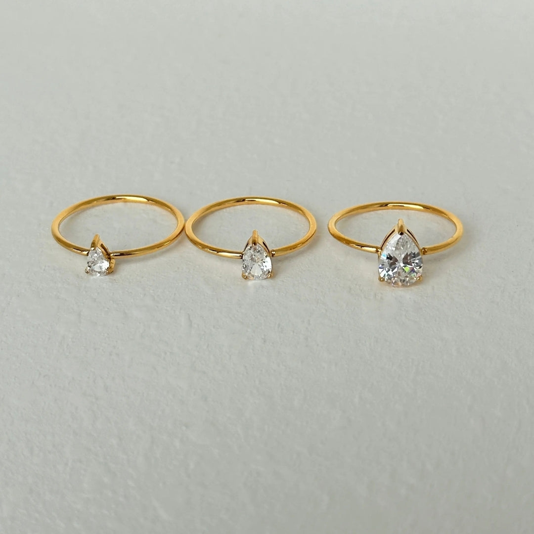 Three gold rings with teardrop-shaped gemstones on a light gray background
