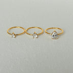 Three gold rings with teardrop-shaped gemstones on a light gray background