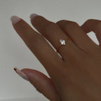 Hand wearing a gold ring with a diamond on a plain background