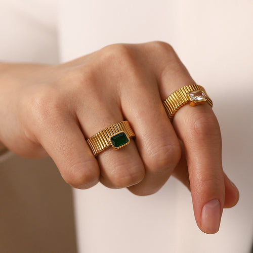 Hand wearing two gold rings with gemstones on a neutral background