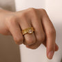 Gold ring with a diamond on a person's finger against a neutral background
