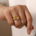 Gold ring with a diamond on a person's finger against a neutral background