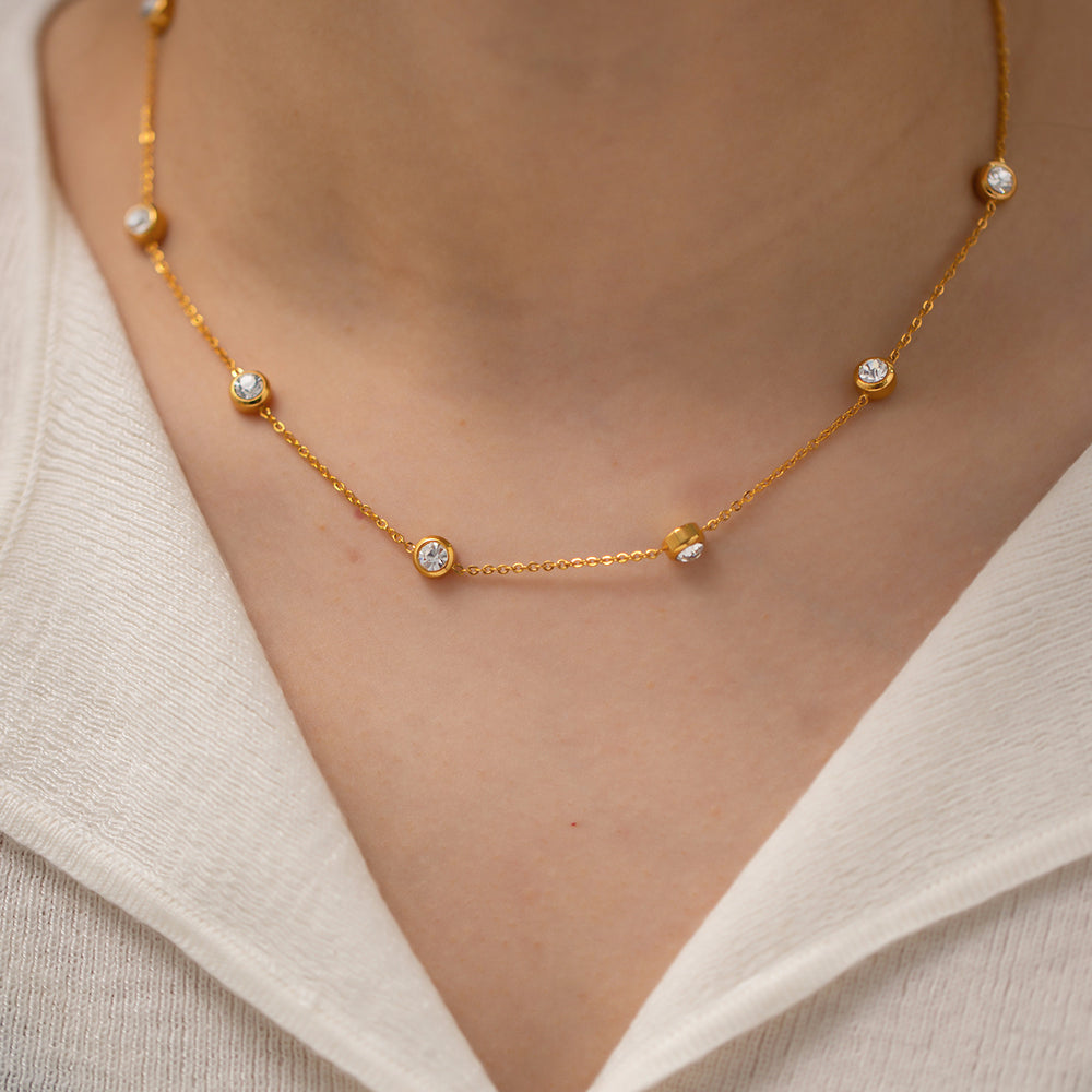 Gold necklace with small diamonds on a person wearing a white top