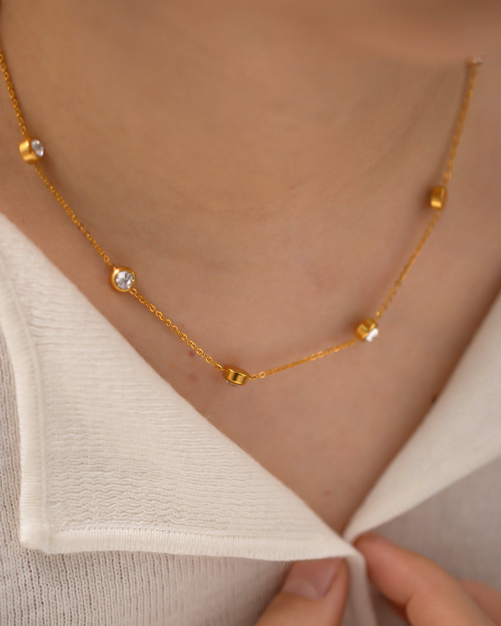Gold necklace with small beads worn by a person wearing a beige top.