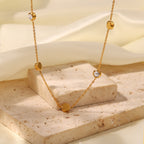 Gold necklace with heart-shaped pendants on a beige stone surface