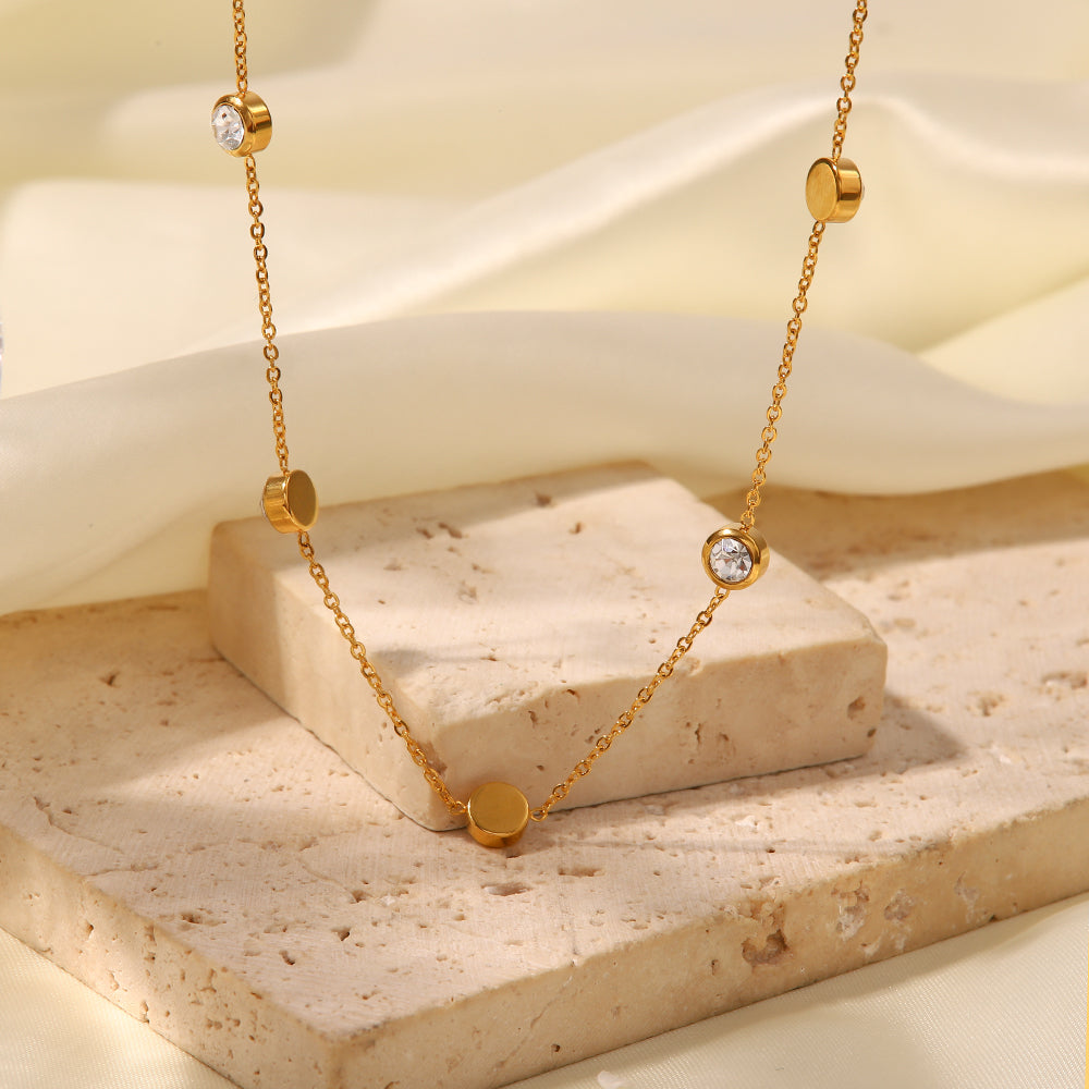 Gold necklace with heart-shaped pendants on a beige stone surface