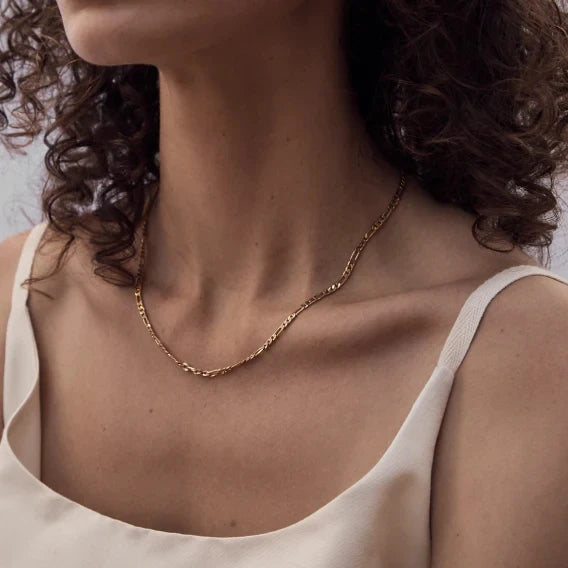 Close-up of a person wearing a gold necklace with a neutral background