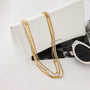 Gold chain necklace draped over a white clutch with sunglasses on a light gray background