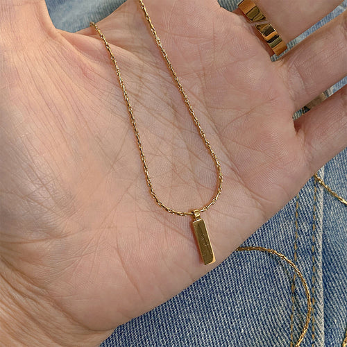 Gold necklace with a pendant on a hand against a denim background
