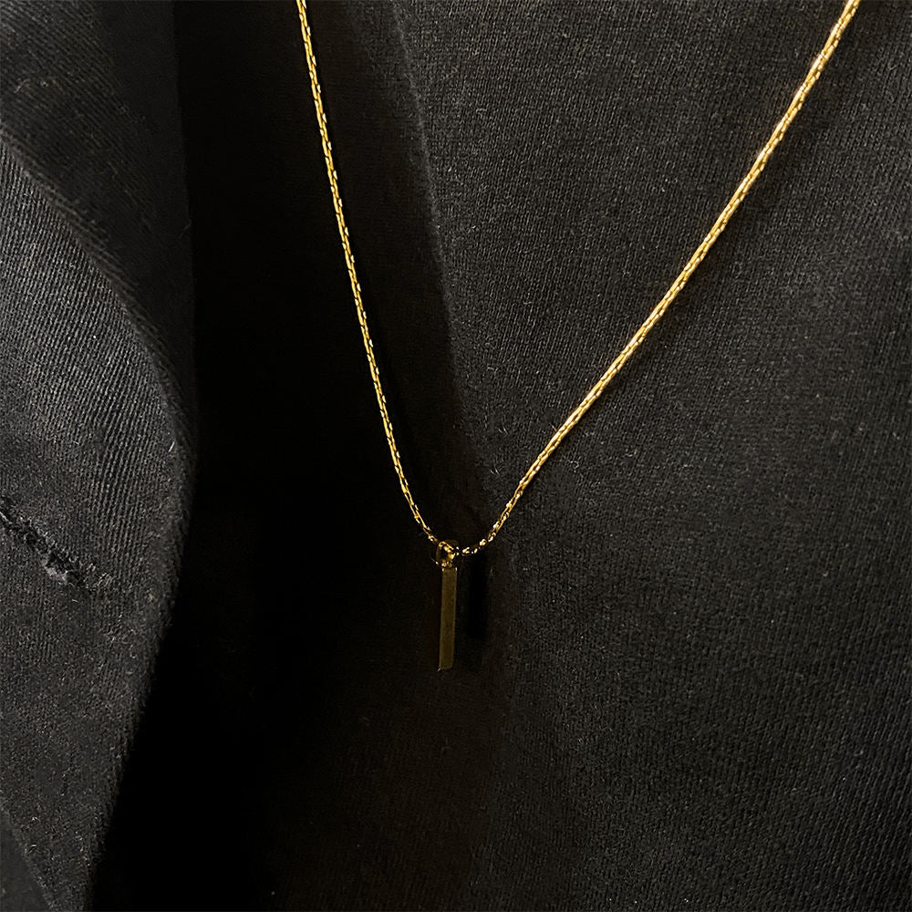 Gold necklace with a small pendant on a black background