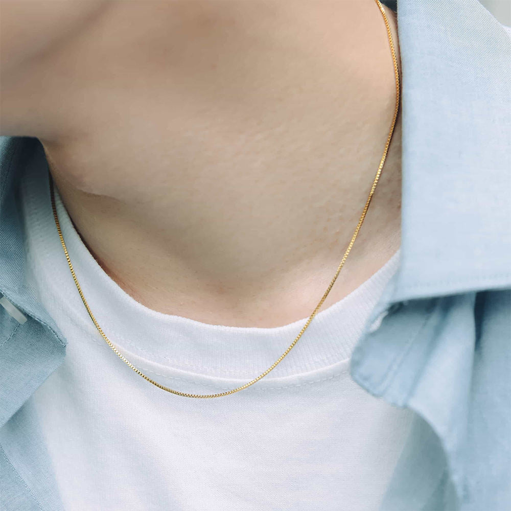 Gold necklace worn by a person with a light blue shirt and white top