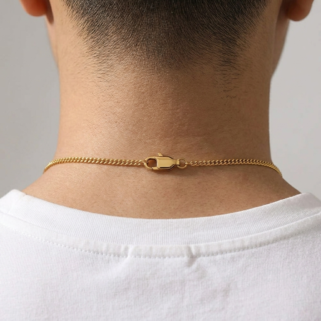 Gold chain necklace on a person wearing a white shirt against a neutral background