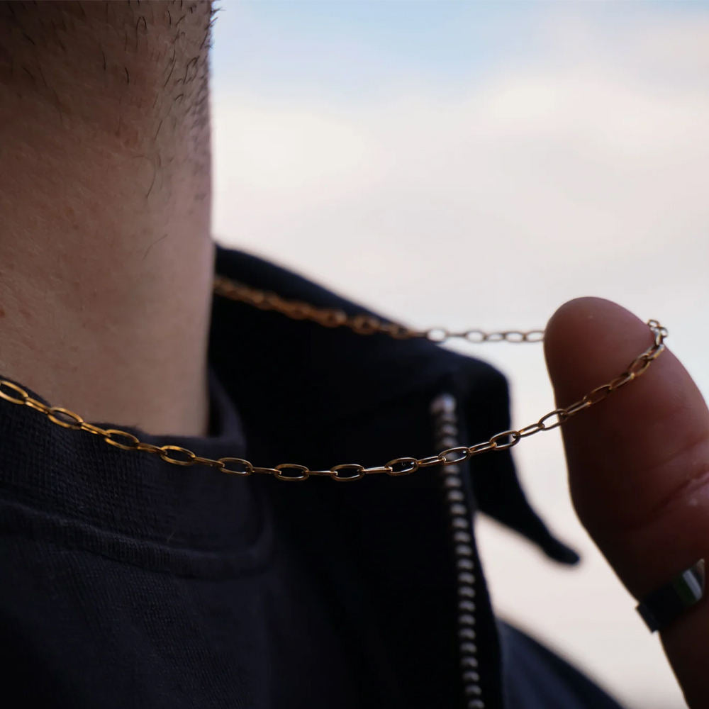 Close-up of a gold chain necklace being held by a person against a blurred background