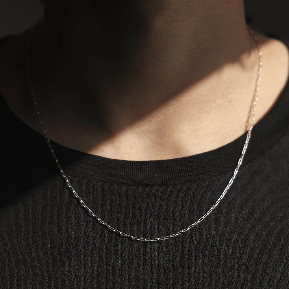 Silver chain necklace worn by a person on a black background
