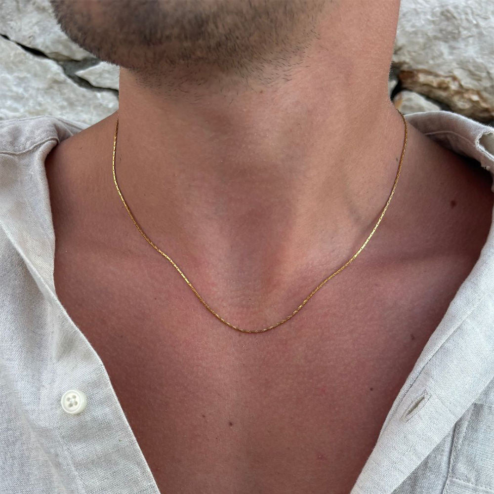 Gold necklace worn by a person with a neutral background