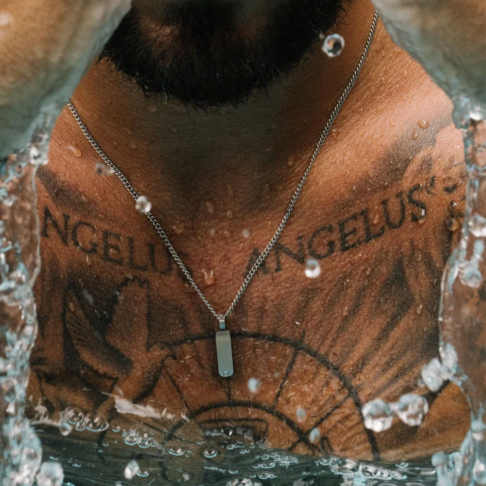 Person with 'ANGELUS' tattoo on neck wearing a necklace with a pendant.