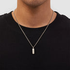 Person wearing a black shirt with a silver necklace featuring a pendant.