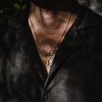 Close-up of a person wearing a black shirt with a gold necklace and visible neck tattoos.