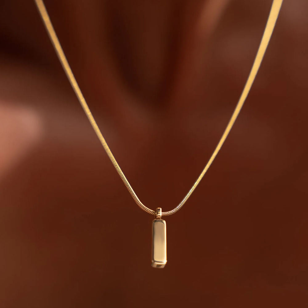 Gold necklace with a rectangular pendant on a brown background