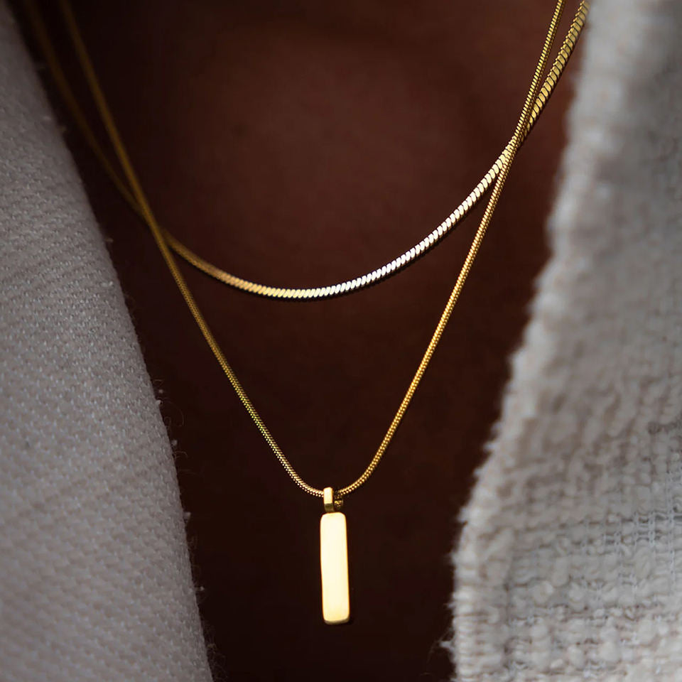 Two gold necklaces with a pendant on a textured surface