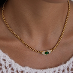 Gold chain necklace with a green gemstone on a person wearing a white lace garment.