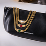 Gold chains with gemstones on a black clutch bag with 'Gentle Monster' branding.