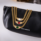 Gold chains with gemstones on a black clutch bag with 'Gentle Monster' branding.