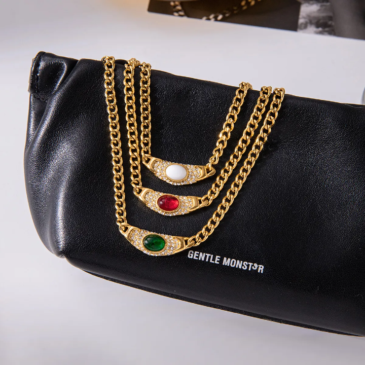 Gold chains with gemstones on a black clutch bag with 'Gentle Monster' branding.