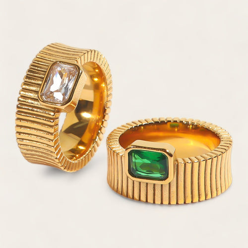 Two gold rings with gemstones on a light gray background
