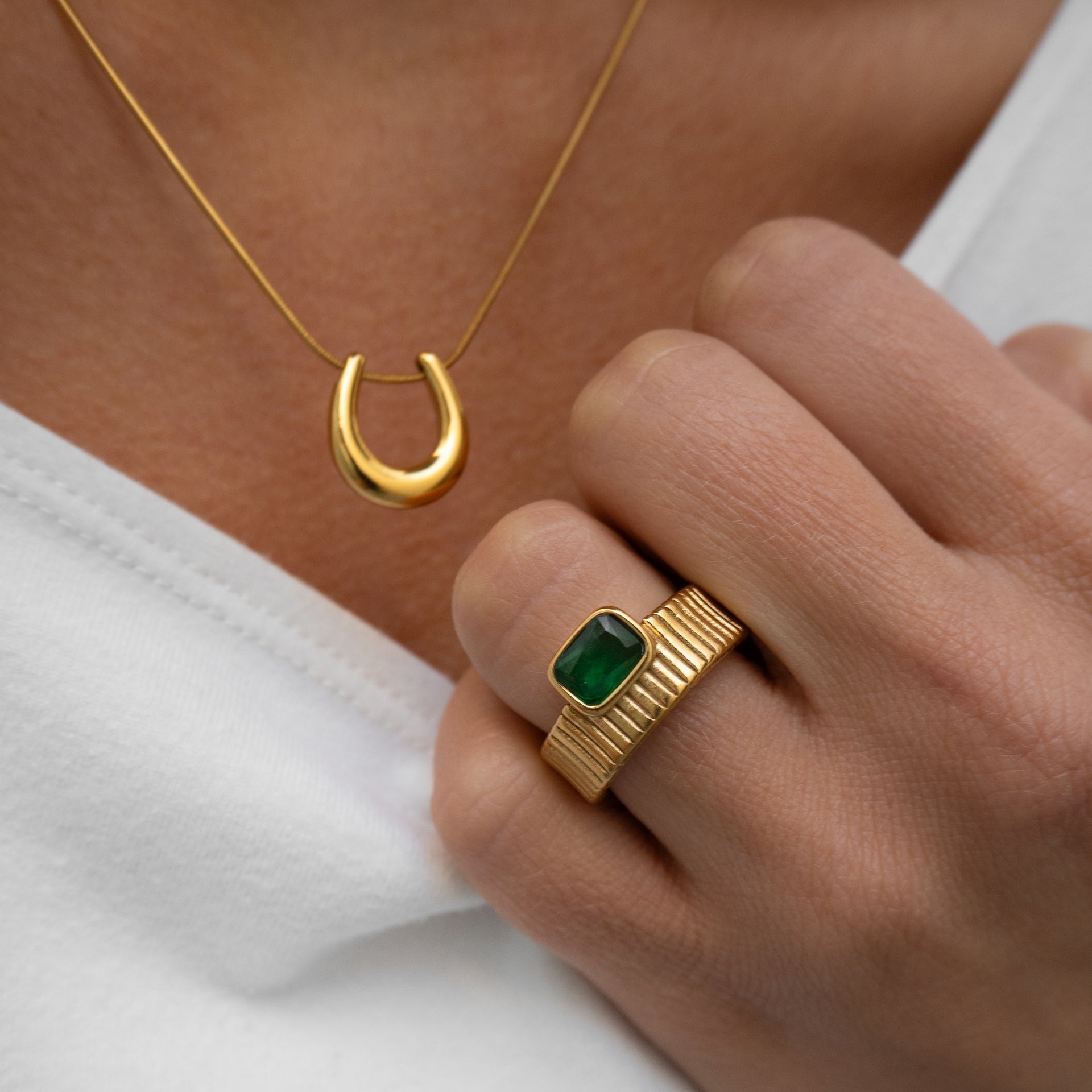 Gold necklace and ring with green gemstone on a white background