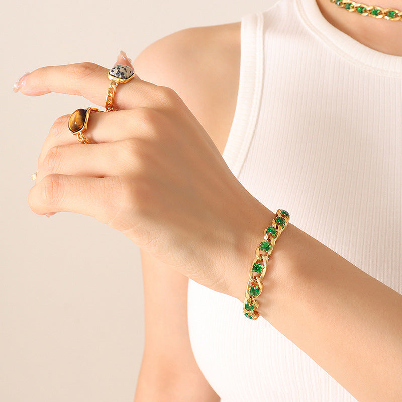 Hand wearing a gold bracelet with green gemstones on a neutral background