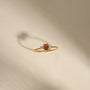 Gold ring with a red gemstone and small diamonds on a beige background