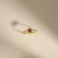 Gold ring with a red gemstone and small diamonds on a beige background