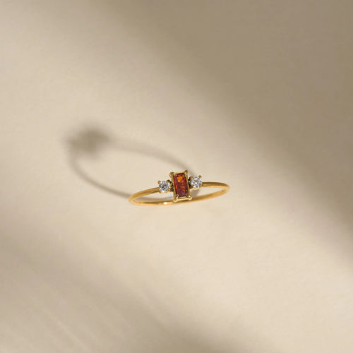Gold ring with a red gemstone and small diamonds on a beige background