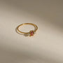 Gold ring with a red gemstone and small diamonds on a beige background