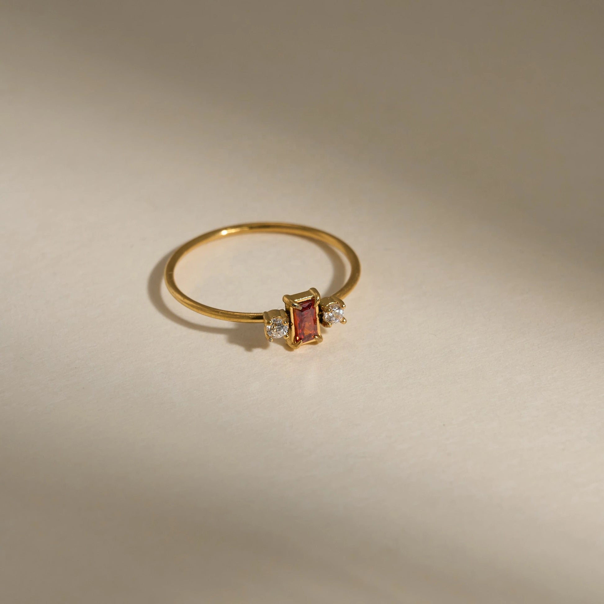 Gold ring with a red gemstone and small diamonds on a beige background