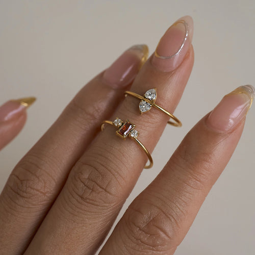 Hand wearing two gold rings with gemstones on a neutral background