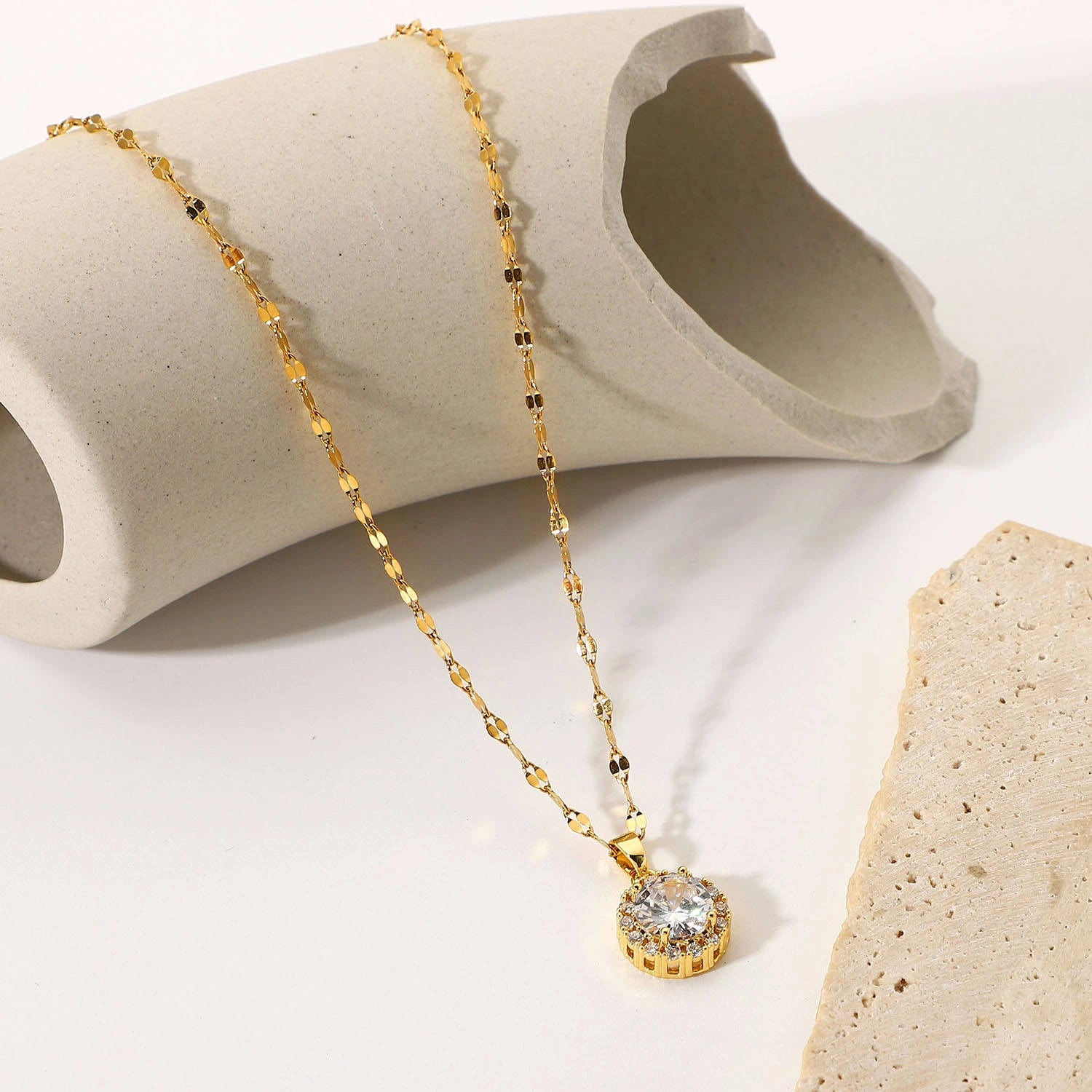 Gold necklace with a diamond pendant on a textured beige surface