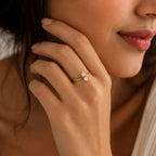 Close-up of a woman's hand wearing a gold ring with a diamond, touching her ear.