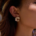 Close-up of an ear wearing a floral gold earring with a blurred background