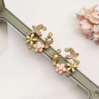Gold and pink floral earrings on a white surface with a shell in the background