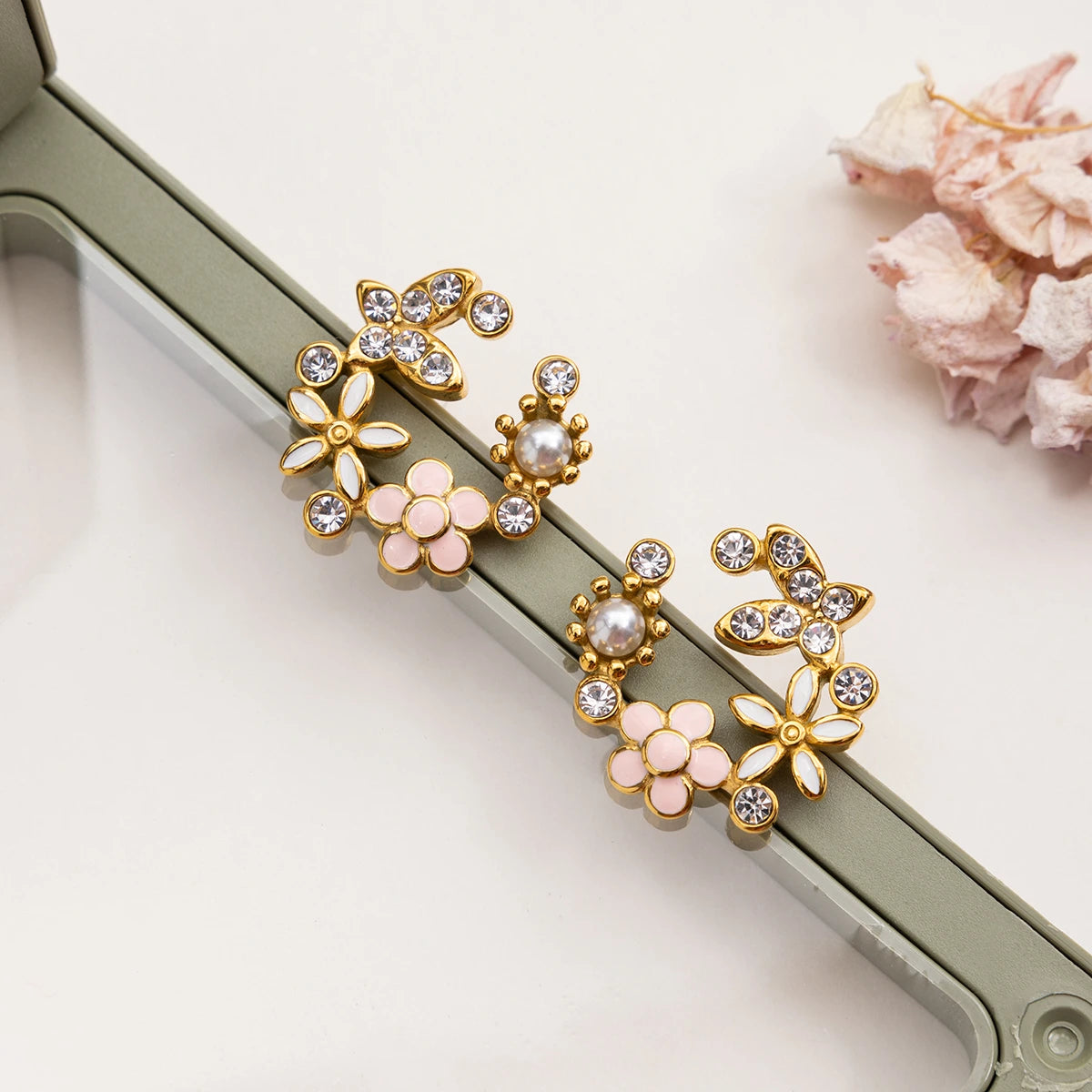 Gold and pink floral earrings on a white surface with a shell in the background